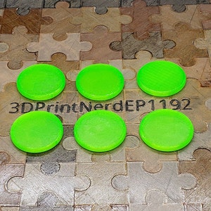 May include: Six bright green round plastic discs, possibly game pieces or tokens, arranged in a semi-circle on a brown jigsaw mat. The text "3DPrintNerdEP1192" is visible in the centre of the image.