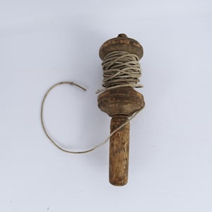 May include: A wooden tool with a handle and a spool for winding string. The spool is filled with a beige string.