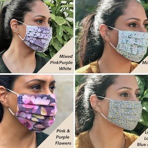 Op de afbeelding: Vier verschillende stoffen mondmaskers met verschillende patronen. De maskers zijn geplooid en hebben elastische oorlussen. De patronen omvatten gemengde roze, paarse en witte bloemen, muntgroene bladeren, roze en paarse bloemen en een blauw en geel bloemenpatroon.