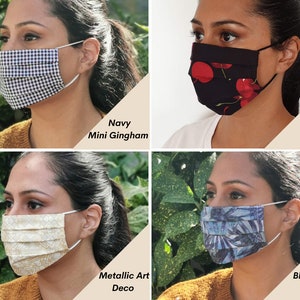 Op de afbeelding: Vier verschillende gezichtsmaskers met verschillende patronen. De maskers zijn geplooid en hebben elastische oorlussen. De patronen omvatten marineblauw mini-gingham, kersenprint, metallic art deco en blauwe palm.