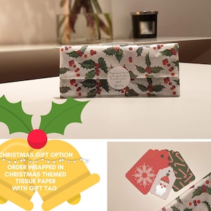 Op de afbeelding: Een kerstcadeau-optie met een witte cadeauzak die is ingepakt in rood en groen stekelbaardmotiefgekleurd tissuepapier. De cadeauzak heeft een witte ronde sticker met tekst. Het cadeau wordt geleverd met een rood-witte sneeuwvlokken-cadeauetiket en een groen-witte pepermuntstok-cadeauetiket.