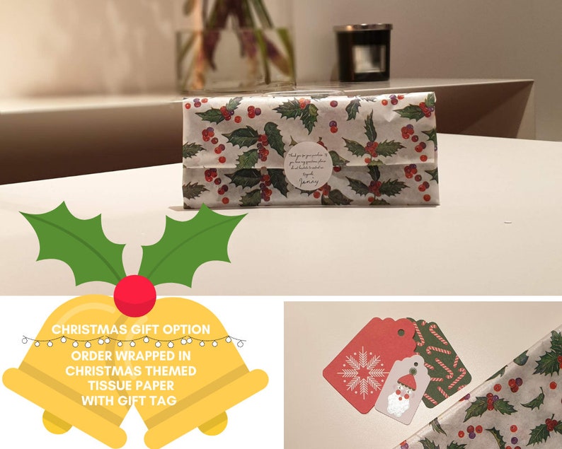 Op de afbeelding: Een kerstcadeau-optie met een witte cadeauzak die is ingepakt in rood en groen stekelbaardmotiefgekleurd tissuepapier. De cadeauzak heeft een witte ronde sticker met tekst. Het cadeau wordt geleverd met een rood-witte sneeuwvlokken-cadeauetiket en een groen-witte pepermuntstok-cadeauetiket.
