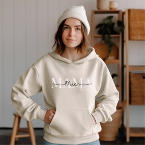 Könnte beinhalten: Ein cremefarbener Hoodie mit dem Aufdruck "MAMA Mia EST 2021" auf der Vorderseite.