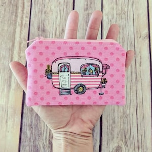 May include: Pink polka dot zippered pouch with a cartoon illustration of a vintage camper with a striped awning and potted plants.