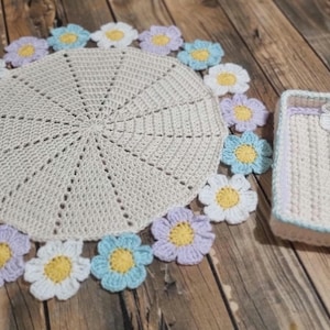 May include: A crocheted table runner with a white center and a border of crocheted flowers in shades of blue, white, and purple. A matching crocheted tray with a similar flower design is also pictured.