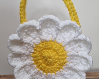 May include: A crocheted daisy-shaped handbag with a yellow handle and a yellow center. The bag is white with a yellow center.