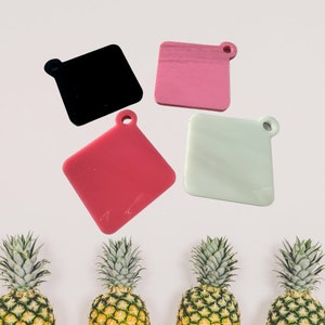 May include: Four square-shaped keychains with different colors. The keychains are black, pink, red, and light green. Each keychain has a small hole at the top for attaching to a key ring.
