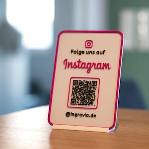 Könnte beinhalten: Weiße Karte mit rosa Umrandung, mit einem QR-Code und dem Text "Folge uns auf Instagram @ingravio.de".