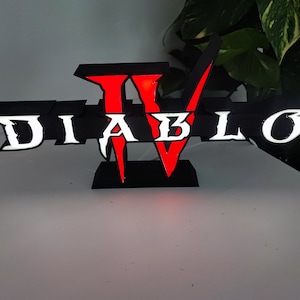 Puede incluir: Un logotipo Diablo IV impreso en 3D en negro y rojo con letras blancas. El logotipo está iluminado desde atrás, creando un efecto brillante.