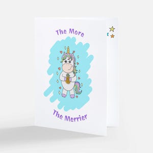 May include: A greeting card with a cartoon unicorn holding a pineapple. The card has a blue background with white hearts and stars. The text on the card reads "The More The Merrier".