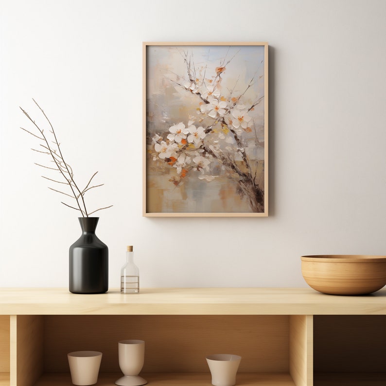 May include: A framed painting of a white flower branch with a light brown background. The painting is hanging on a white wall above a wooden shelf with a black vase, a clear glass bottle, and a wooden bowl.