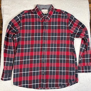 May include: Red, black, and white plaid button-down shirt. The long-sleeved shirt has a button-down collar and a chest pocket. The shirt is made of a soft, woven fabric. The brand name is visible on the collar.