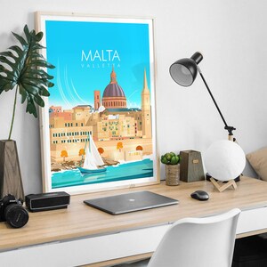 May include: A framed print of a colorful illustration of the city of Valletta, Malta. The print features a blue sky, a sailboat in the water, and the city's iconic buildings, including the dome of St. John's Co-Cathedral. The text "MALTA VALLETTA" is printed at the top of the print.