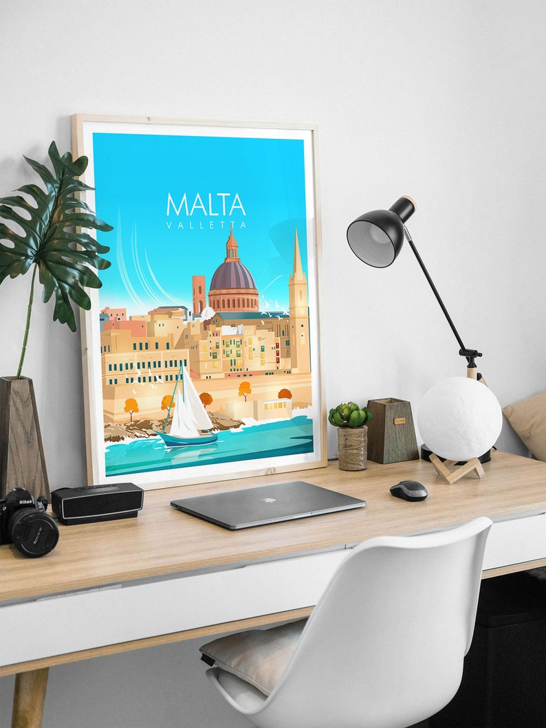 May include: A framed print of a colorful illustration of the city of Valletta, Malta. The print features a blue sky, a sailboat in the water, and the city's iconic buildings, including the dome of St. John's Co-Cathedral. The text "MALTA VALLETTA" is printed at the top of the print.