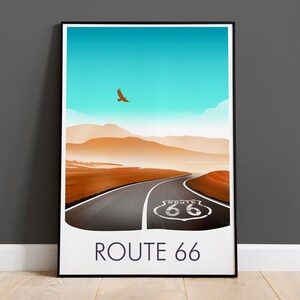 May include: A poster with a minimalist design featuring a road leading into a desert landscape with a blue sky and a single bird flying overhead. The road has a white "Route 66" sign in the middle of the road. The poster has a white border and black frame. The text "ROUTE 66" is printed in blue at the bottom of the poster.