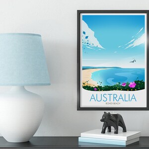 May include: A framed poster featuring a colourful illustration of Bondi Beach in Australia. The poster depicts a blue sky, white clouds, a blue ocean, a sandy beach, and green foliage with pink flowers. The text on the poster reads "Australia Bondi Beach".