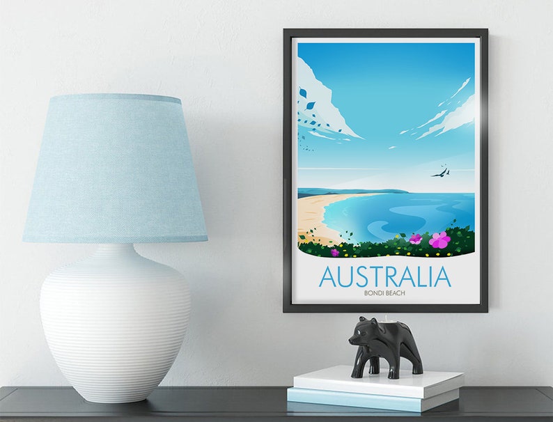 May include: A framed poster featuring a colourful illustration of Bondi Beach in Australia. The poster depicts a blue sky, white clouds, a blue ocean, a sandy beach, and green foliage with pink flowers. The text on the poster reads "Australia Bondi Beach".