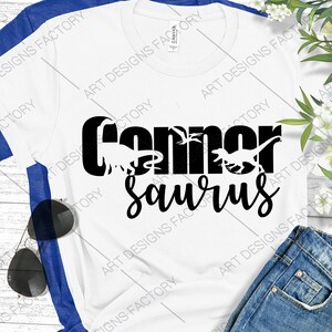 May include: White t-shirt with black text that reads "Conner Saurus" with dinosaur silhouettes.