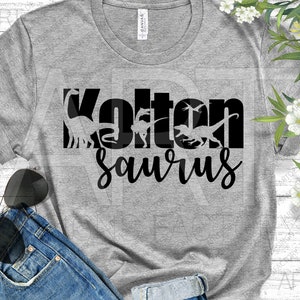May include: A grey t-shirt with black text that reads "Kolton Saurus" with dinosaur silhouettes inside the letters.