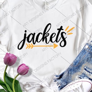 Puede incluir: Camiseta blanca con el texto "jackets" en letra negra con una flecha amarilla apuntando hacia la derecha. La camiseta está sobre una superficie de madera con unos pantalones cortos de mezclilla y una zapatilla blanca.