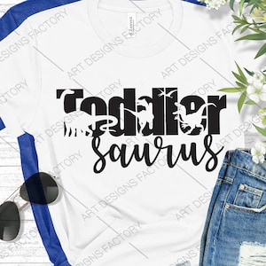 May include: White t-shirt with black text that reads "Toddler Saurus" with dinosaur silhouettes inside the letters.