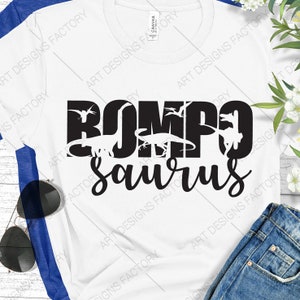 May include: White t-shirt featuring a black graphic design that reads "ROMPOsaurus" with dinosaur silhouettes incorporated into the letters.
