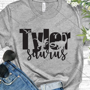 May include: Grey t-shirt with black text that reads "Tyler Saurus" with dinosaur silhouettes inside the letters.