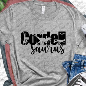 May include: Grey t-shirt with black text that reads "Corden Saurus" with dinosaur silhouettes in the text.