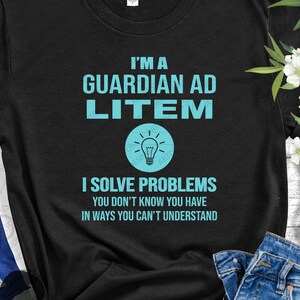 Puede incluir: Camiseta negra con el texto "Soy un tutor ad litem. Resuelvo problemas que no sabes que tienes de maneras que no puedes entender." y un gráfico de bombilla azul claro.