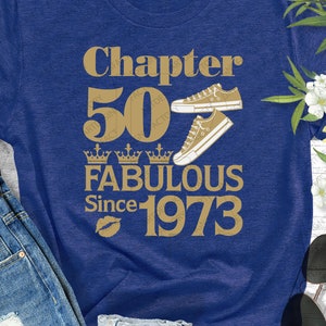 May include: A blue t-shirt with gold text that reads "Chapter 50 Fabulous Since 1973". The text is surrounded by four gold crowns and two gold sneakers.