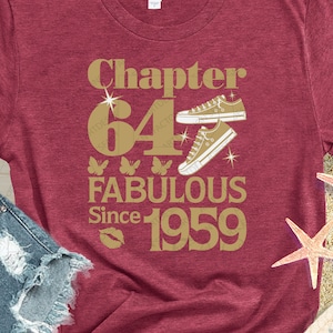 Puede incluir: Camiseta color burdeos con texto dorado que dice "Chapter 64 Fabulous Since 1959". El texto está rodeado de mariposas y un par de zapatillas doradas.