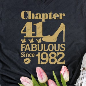 Puede incluir: Camiseta negra con texto dorado que dice "Chapter 41 Fabulous Since 1982". El texto está decorado con un zapato de tacón alto, mariposas y una huella de labios.