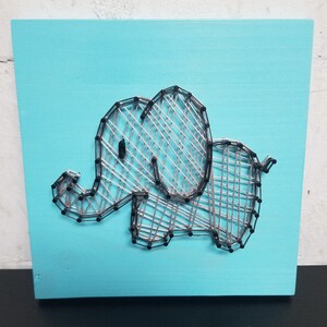 May include: A gray string art elephant on a light blue wooden background.