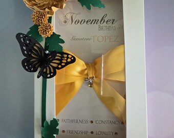 May include: A white card with a window showing a yellow bow, a black butterfly, and green leaves. The card says "November Birthday Gemstone Topaz" and "Faithfulness, Constancy, Friendship, Loyalty".