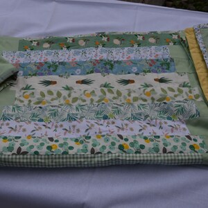 May include: A handmade quilt with a patchwork design featuring various floral and botanical patterns in shades of green, white, and blue. The quilt has a light green border and a yellow binding. The quilt is made of fabric.