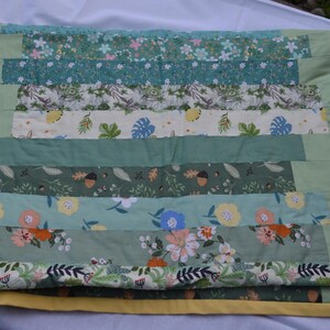 May include: A handmade quilt with a patchwork design. The quilt features horizontal stripes of various floral and leaf patterns in shades of green, blue, and cream. The edges are a solid light green, and the quilt is approximately 60 inches wide and 80 inches long.