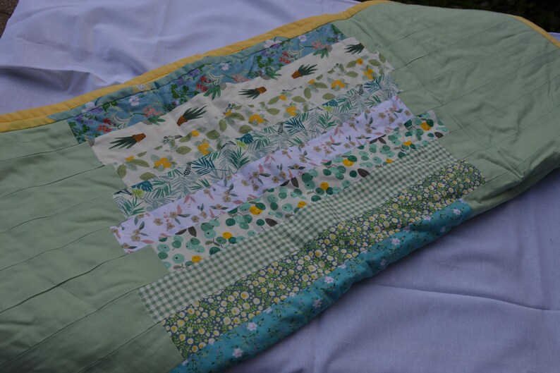 May include: A handmade quilt featuring a patchwork design with various floral and geometric patterns in shades of green, white, and blue. The quilt has a light green base and a yellow border.