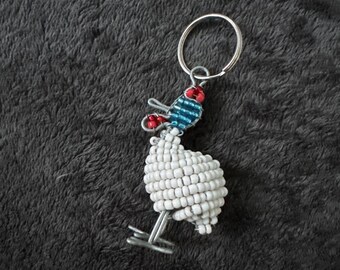 May include: White beaded chicken keychain with a blue and red beaded head and a silver ring.
