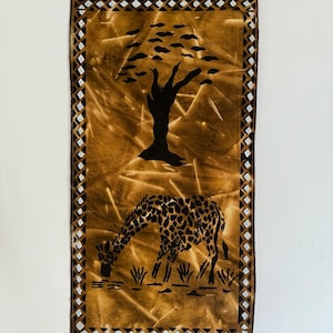 Könnte beinhalten: Ein brauner Wandbehang aus Stoff mit einer schwarzen Silhouette eines Baumes und einer Giraffe, die an einer Wasserstelle trinkt. Der Stoff hat einen geometrischen Muster-Rand.