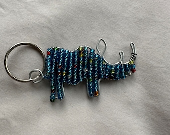 May include: A blue beaded rhinoceros keychain with a silver ring. The rhinoceros is made of wire and has a beaded body.