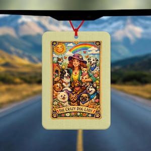 Puede incluir: Ambientador rectangular con una colorida ilustración de una mujer rodeada de perros, un arcoíris y el texto "THE CRAZY DOG LADY". El ambientador cuelga de una cuerda roja, con un fondo de montaña y carretera.