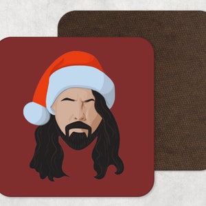 May include: Square coaster with a cartoon illustration of a person with long black hair and a beard wearing a Santa hat. The coaster has a red background. A second brown coaster is next to it.