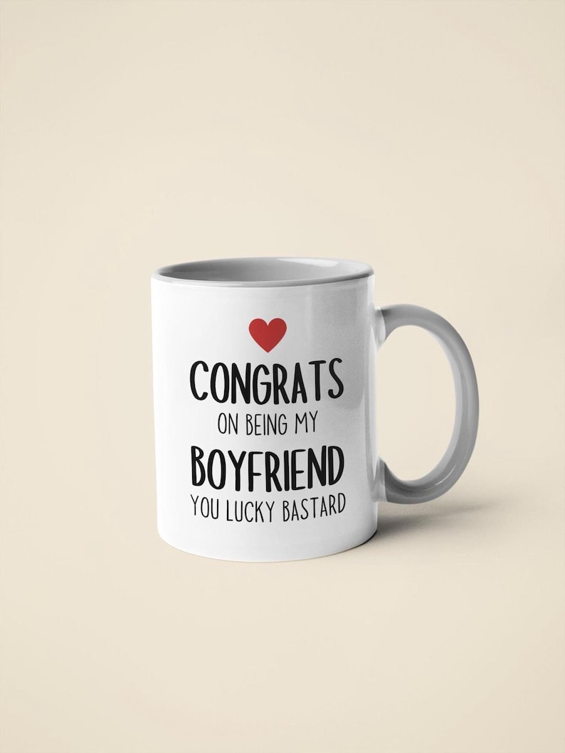 A white ceramic mug with black text that reads "CONGRATS ON BEING MY BOYFRIEND YOU LUCKY BASTARD" and a red heart symbol.