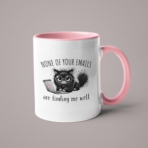 May include: White ceramic mug with a pink interior and handle. The mug features a cartoon cat wearing glasses and using a laptop. Text on the mug reads "NONE OF YOUR EMAILS are finding me well."