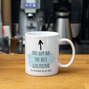 Pode incluir: Caneca de cer&acirc;mica branca com uma seta preta apontando para cima e o texto "Este cara tem a melhor namorada (sim, ela me comprou esta caneca)".