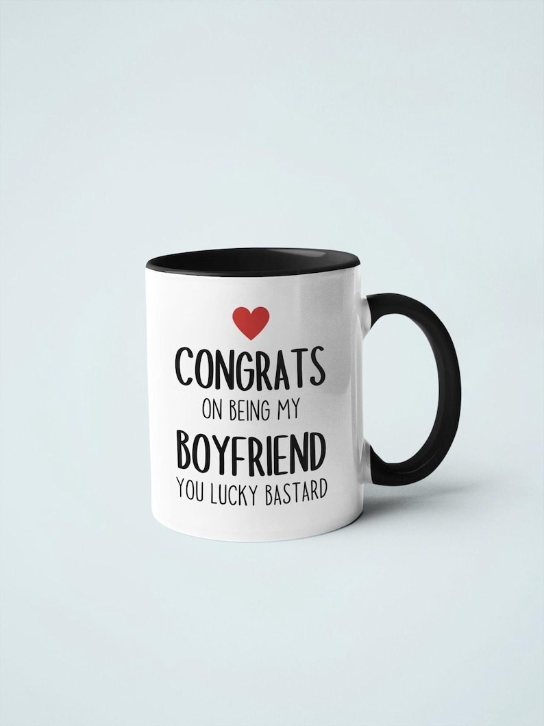 A white mug with black text and a red heart symbol, which reads "CONGRATULATIONS ON BEING MY BOYFRIEND YOU LUCKY BASTARD".