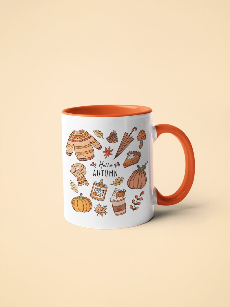 May include: White ceramic mug with an orange interior and handle. The mug is decorated with autumn-themed illustrations, including a sweater, pumpkin, leaves, and the text "Hello Autumn".
