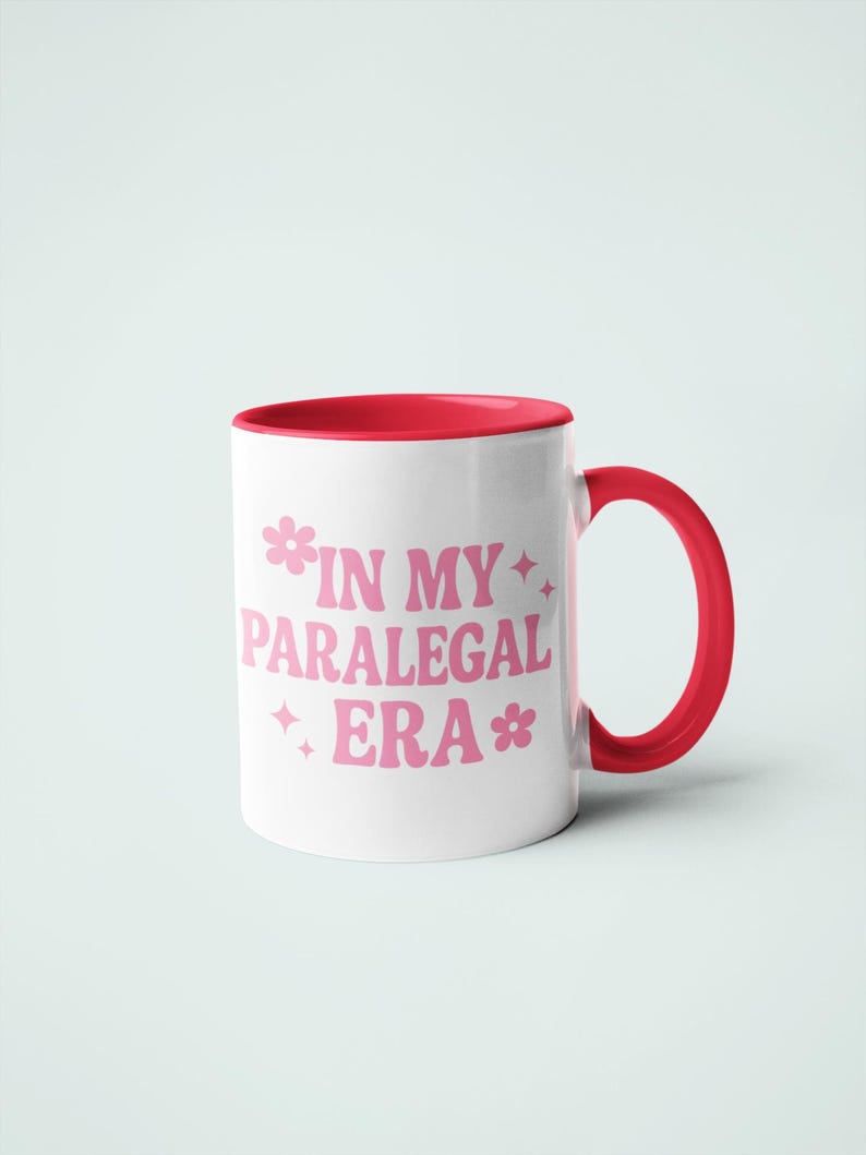 Op de afbeelding: Witte keramische mok met een rode binnenkant en handvat. De mok heeft de tekst "IN MY PARALEGAL ERA" in roze, met bloem- en steraccenten. Een eenvoudig, maar stijlvol ontwerp.