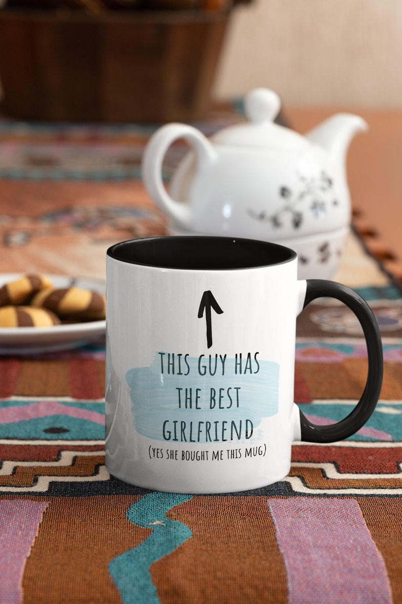 Pode incluir: Caneca de caf&eacute; branca com borda e al&ccedil;a pretas. A caneca tem um fundo de aquarela azul com o texto "Este cara tem a melhor namorada (sim, ela me comprou esta caneca)".