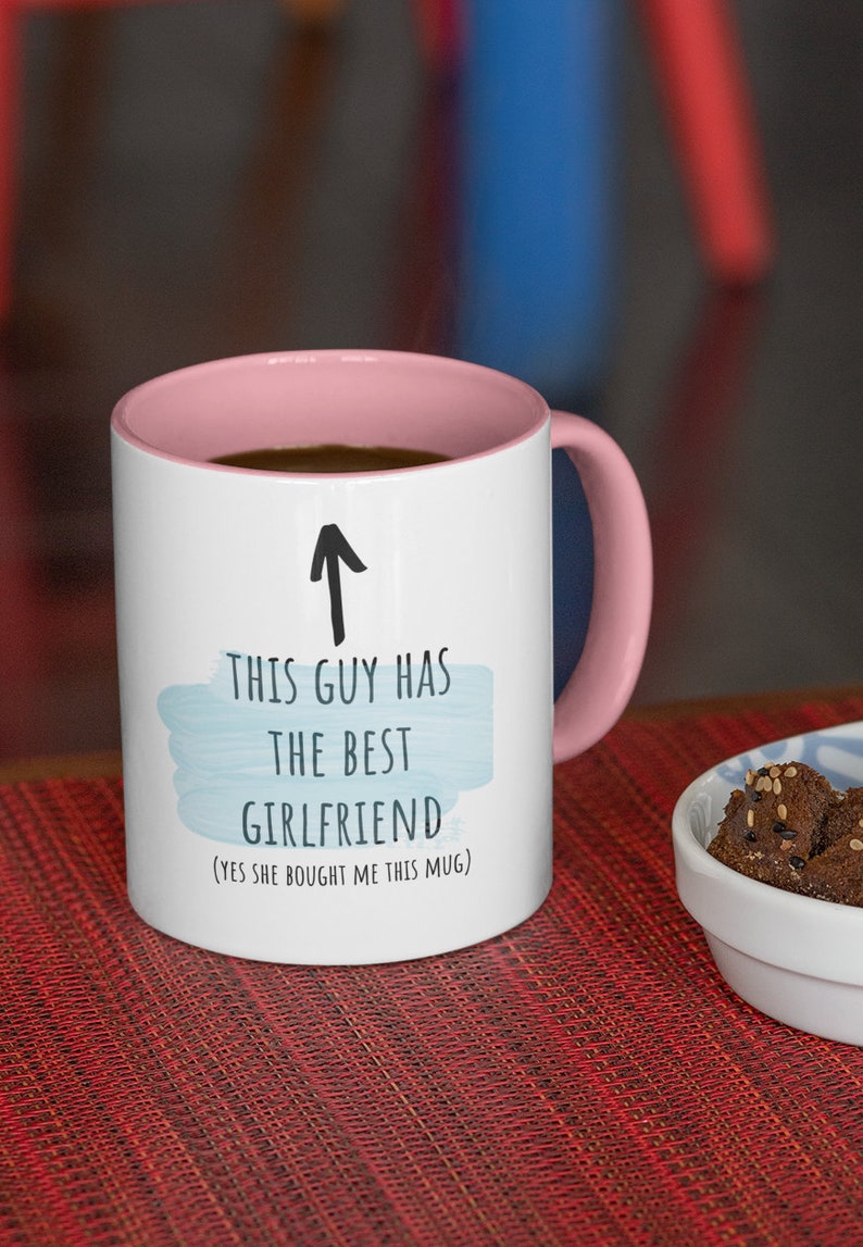 Pode incluir: Caneca de cer&acirc;mica branca com borda e al&ccedil;a rosa. A caneca tem um design de aquarela azul e texto preto que diz "Este cara tem a melhor namorada (Sim, ela me comprou esta caneca)".